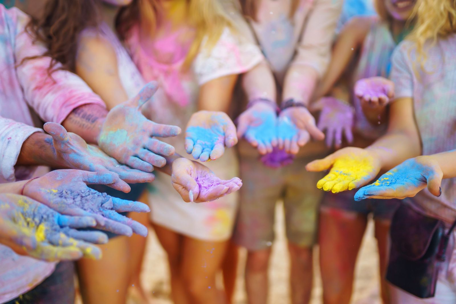 A group of people stand close together holding out open hands covered in blue, purple and yellow coloured powder.