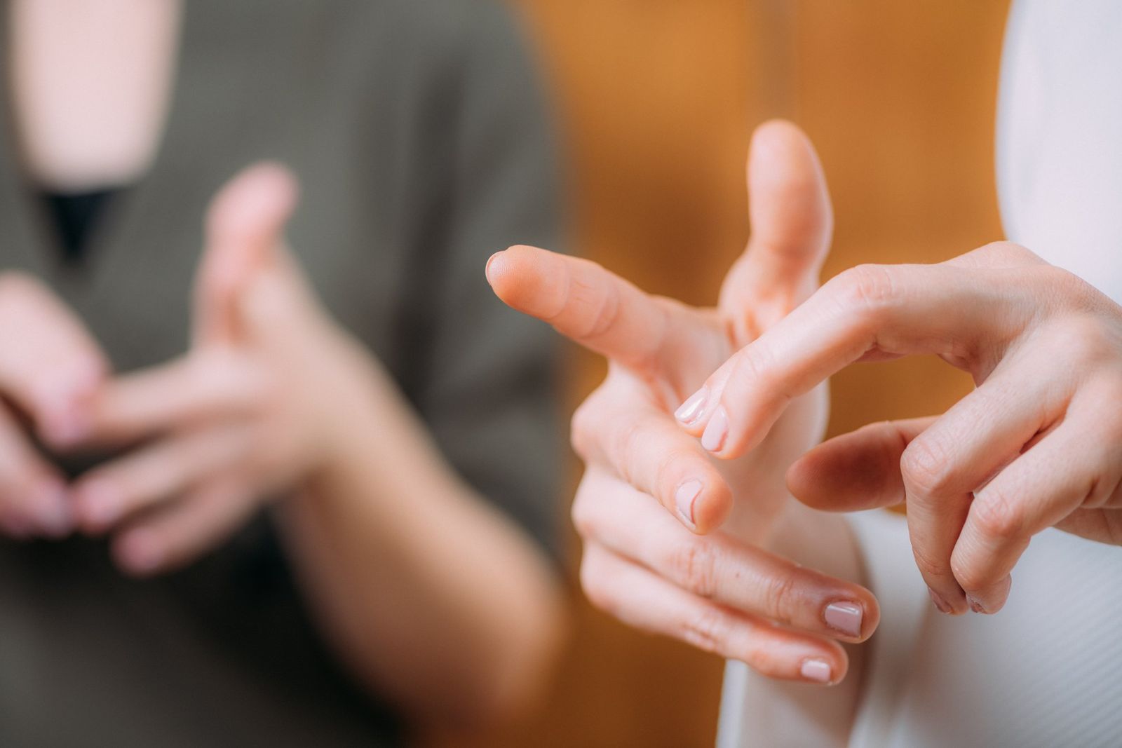 Close view of two people's hands mid-gesture as they sign to each other, one pair sharply in focus and the other blurred.