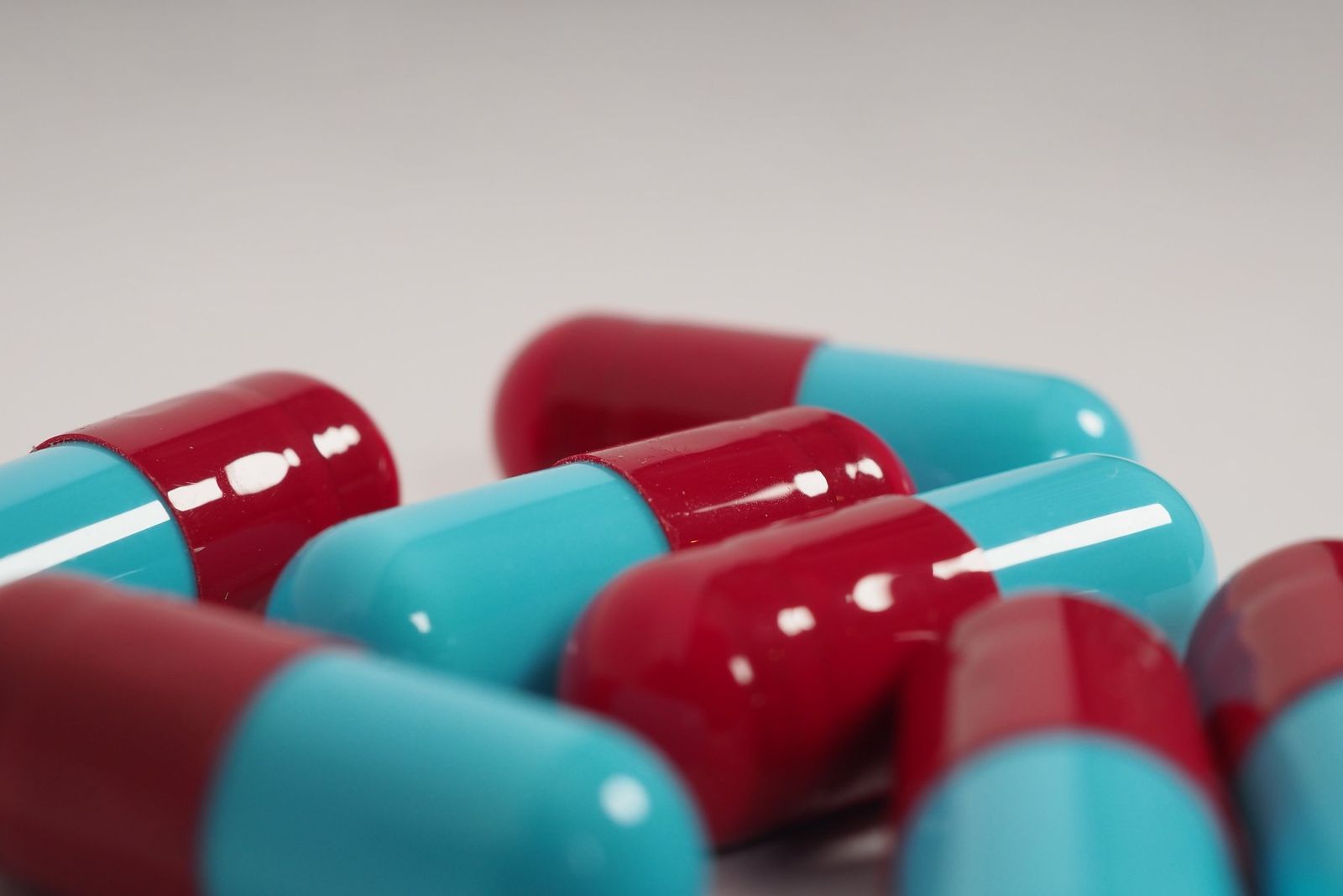 Close-up of several glossy red and teal capsules lying together on a pale surface.